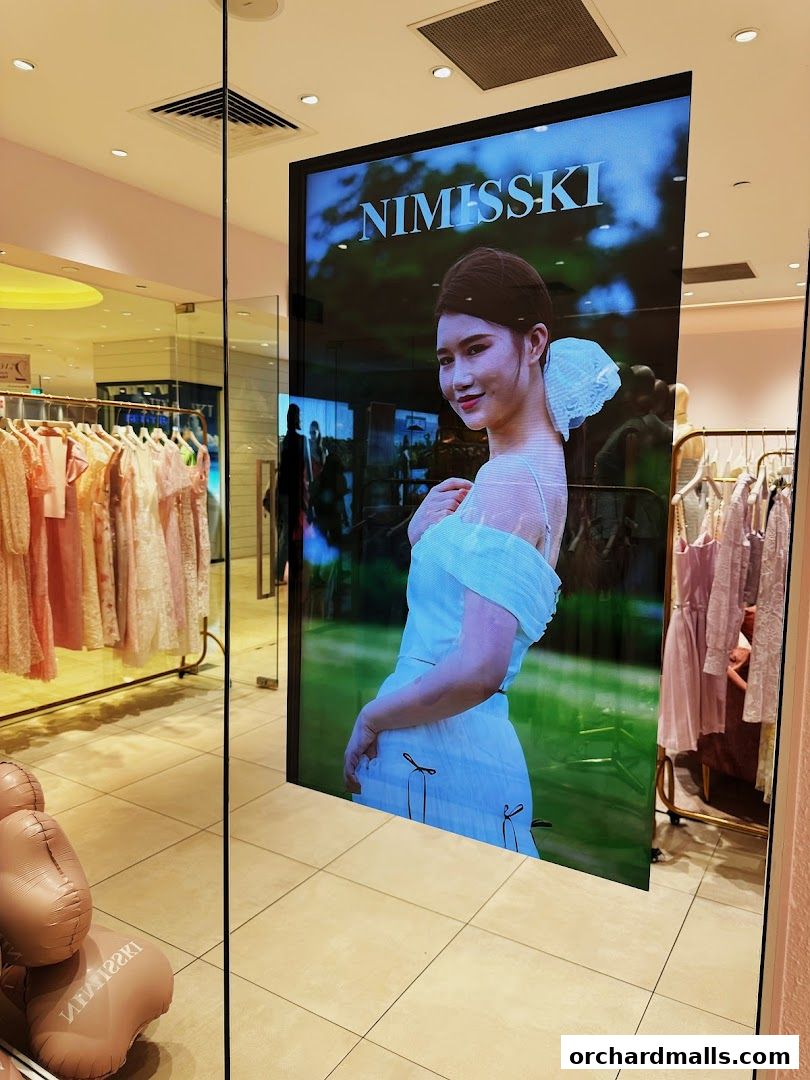 A digital display shows a model wearing a white dress with the brand name NIMISSKI.