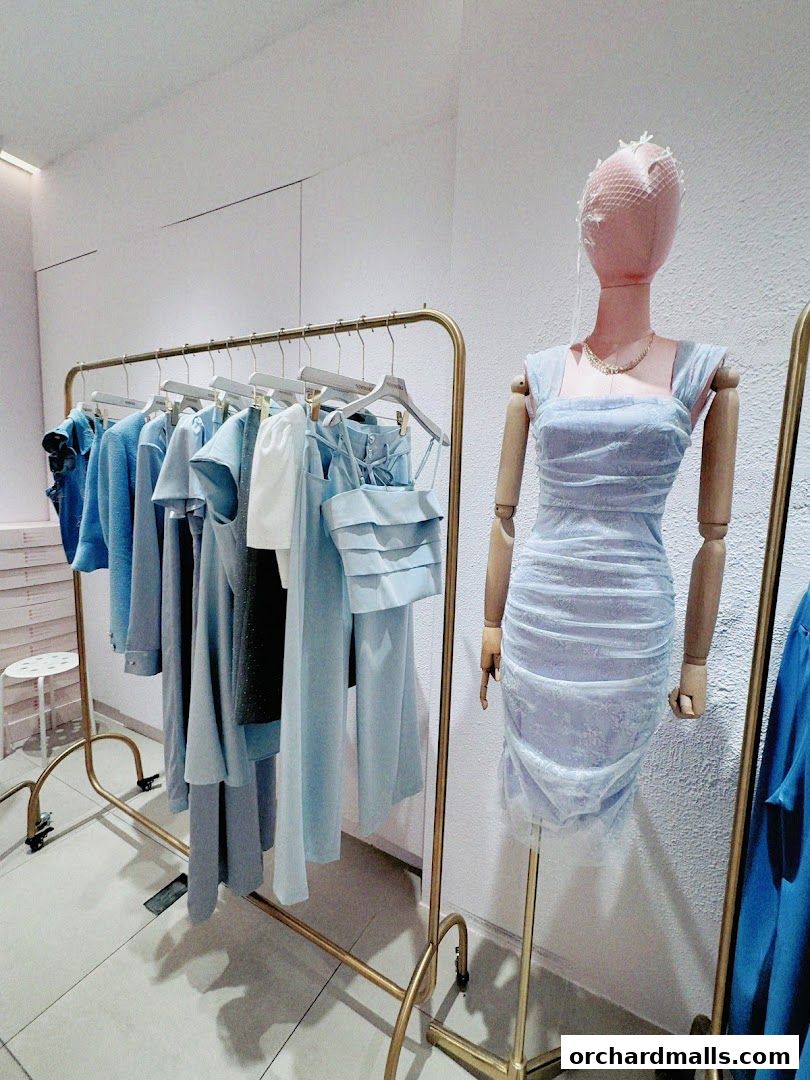 A mannequin displays a light blue ruched dress next to a rack of blue clothing.