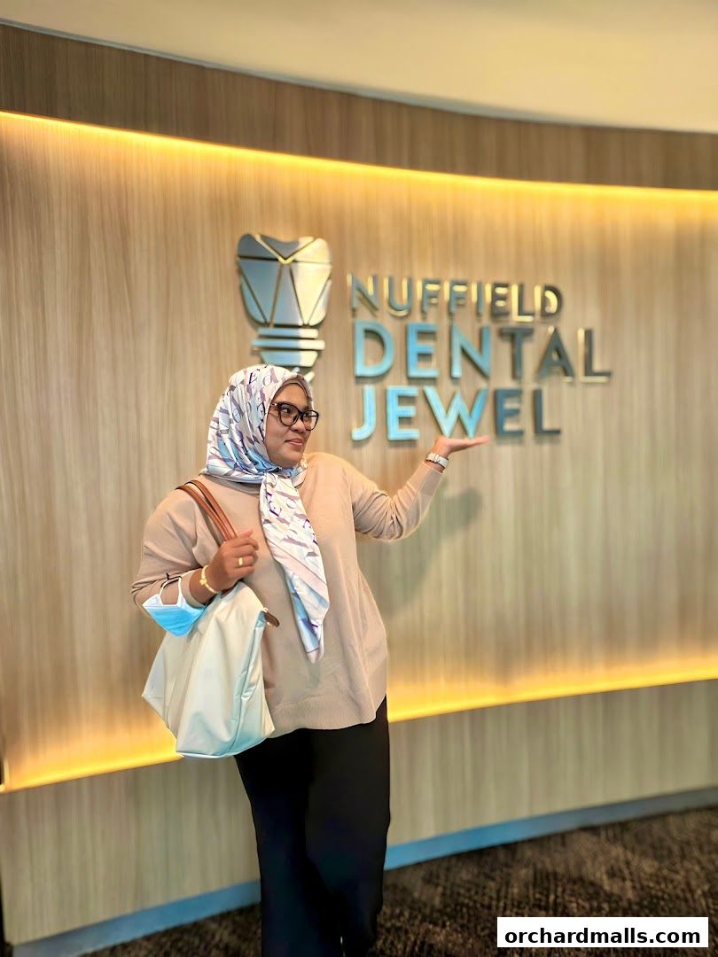 A woman stands in front of the Nuffield Dental Jewel logo, gesturing towards it.
