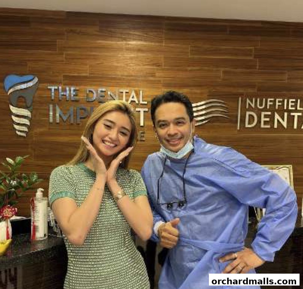A woman and a dentist smile at the camera in front of a dental clinic's signage.