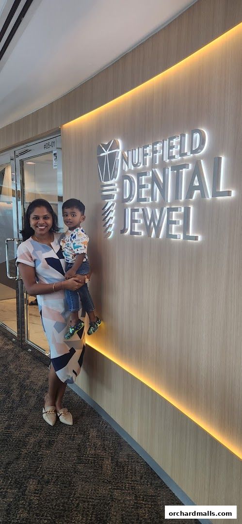 A woman holds a child in front of the Nuffield Dental Jewel signage.