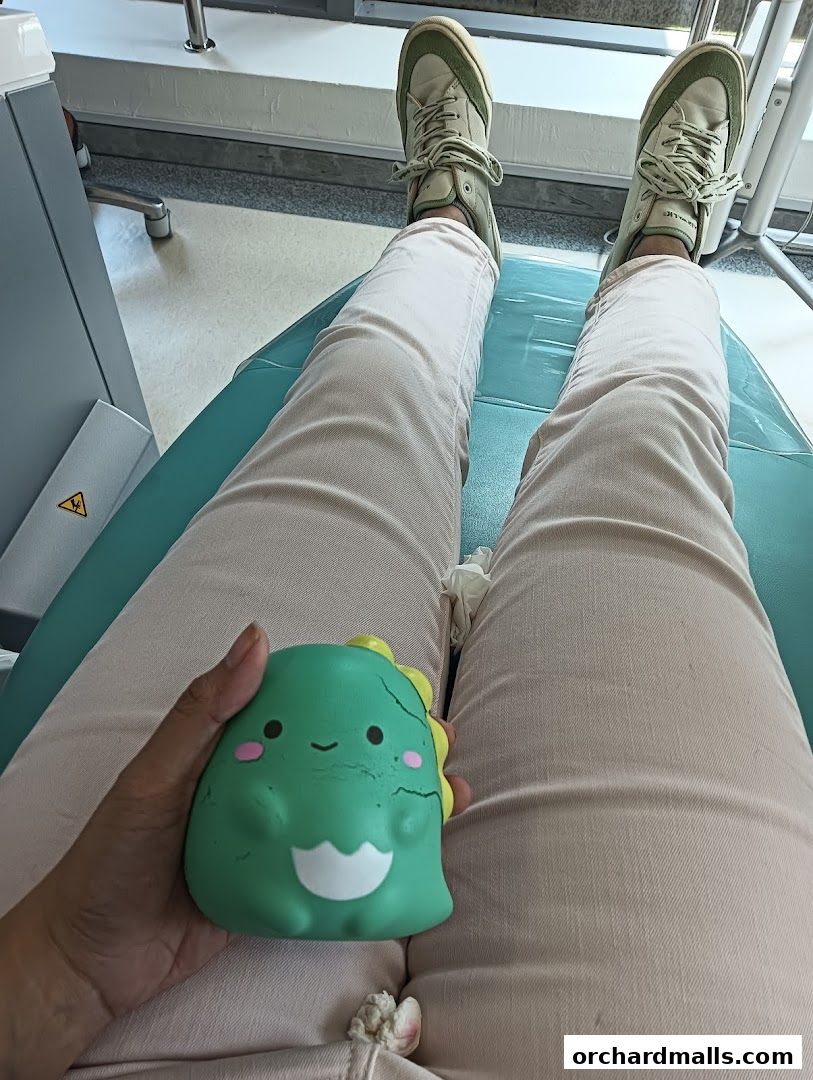 A person's legs and a cute dinosaur toy are shown while sitting on a teal chair.