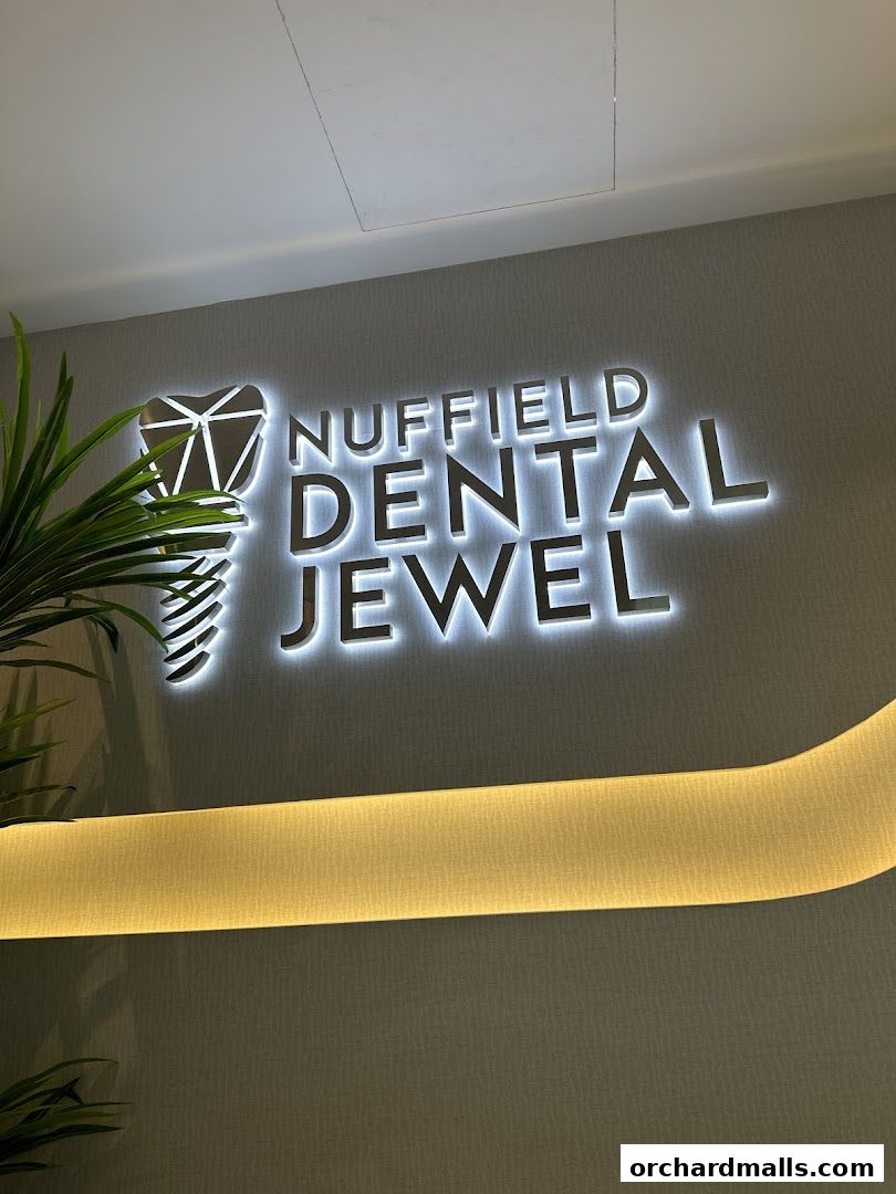 Illuminated sign for Nuffield Dental Jewel with a plant in the foreground.