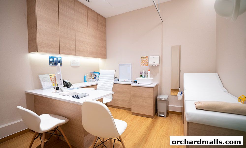 A clean and modern medical examination room with a desk, chairs, and examination bed.