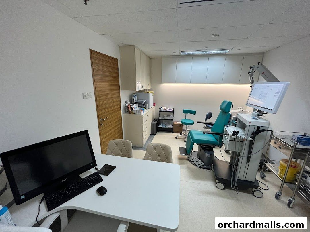 A medical consultation room with a patient chair, examination equipment, and a desk with a computer.