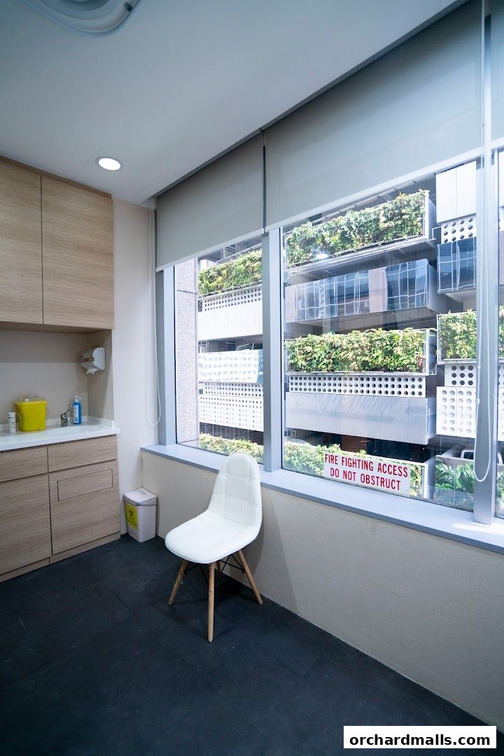 Interior of a medical clinic with a waiting chair and a view of a green wall outside.