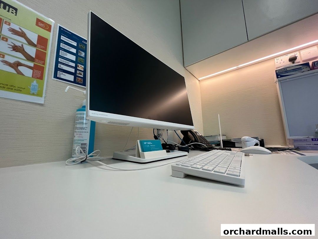 A clean medical clinic desk with a computer, keyboard, and hand sanitizer.