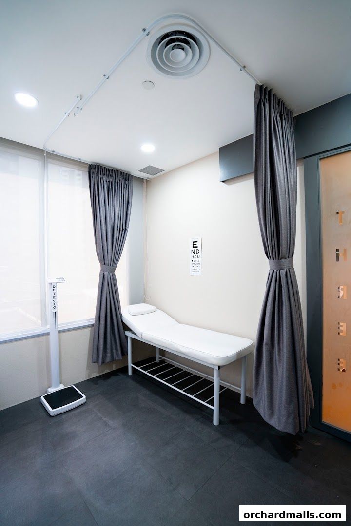A clean medical examination room with a bed, scale, and eye chart.