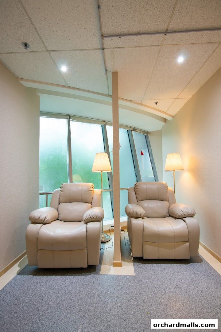 Two comfortable recliners with lamps in a waiting area with large windows.