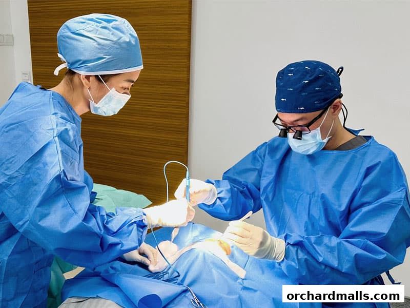 Two surgeons in blue scrubs and masks perform a medical procedure.