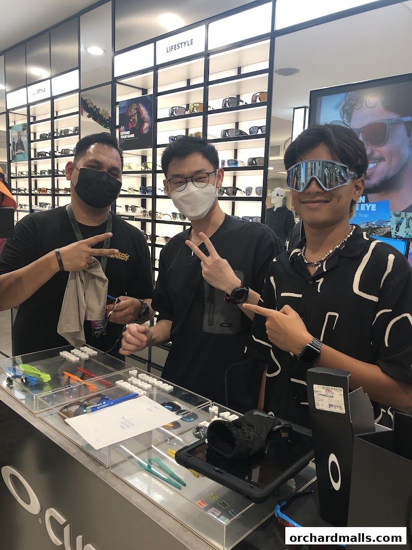 Three people posing in an Oakley store with sunglasses displayed.