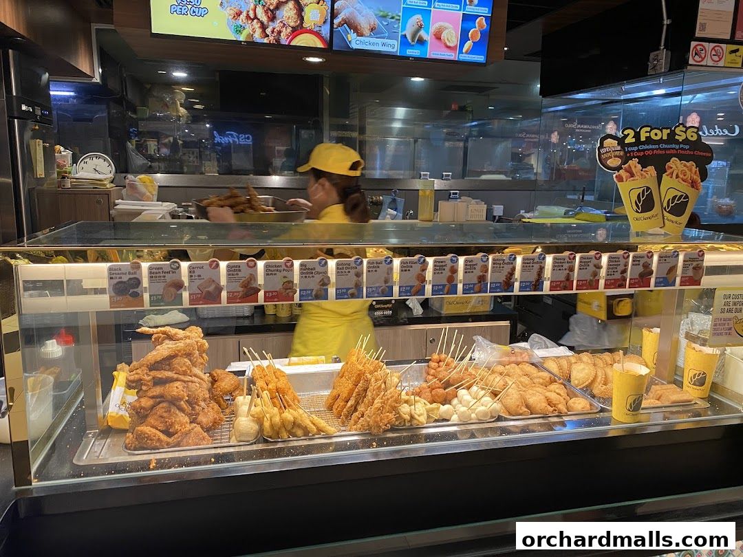 A display of various fried snacks and a worker preparing food at Old Chang Kee.