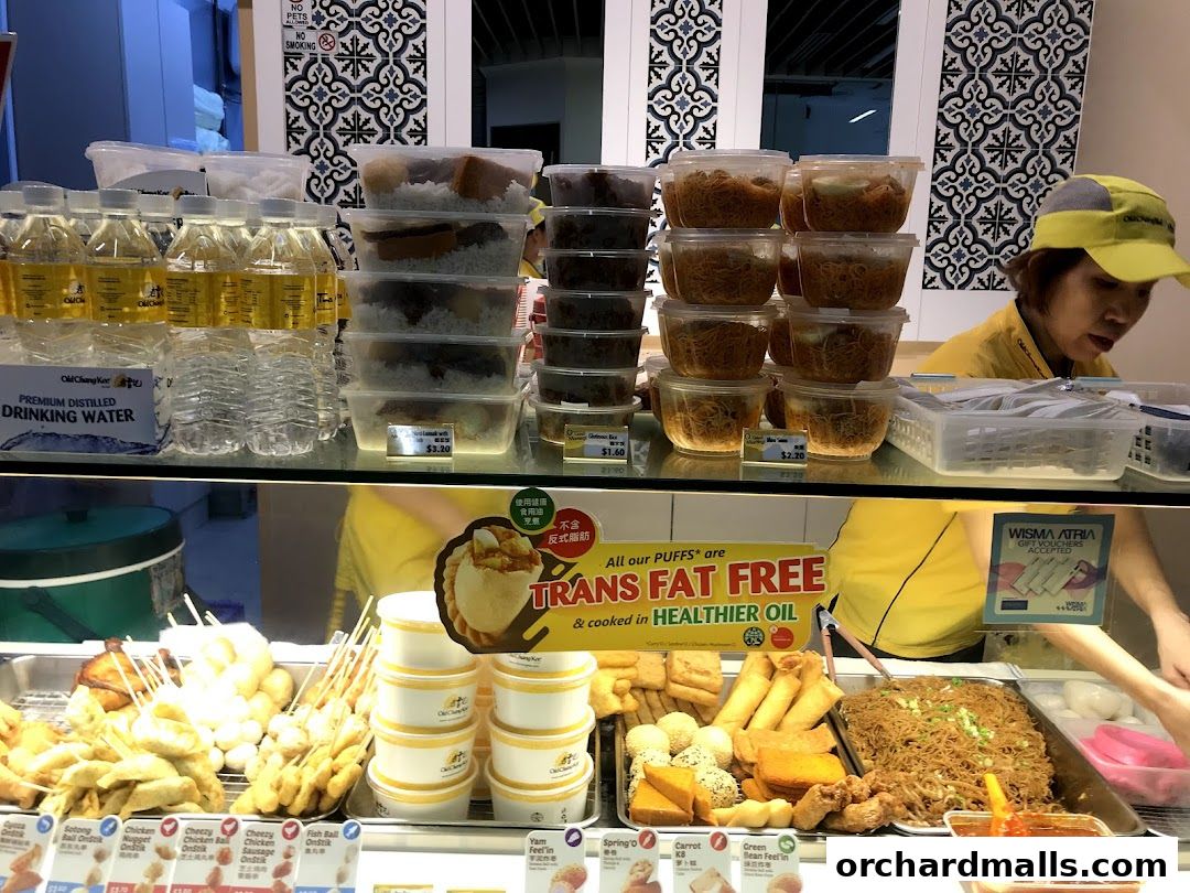 A display of various food items and drinks at Old Chang Kee, with a staff member serving.