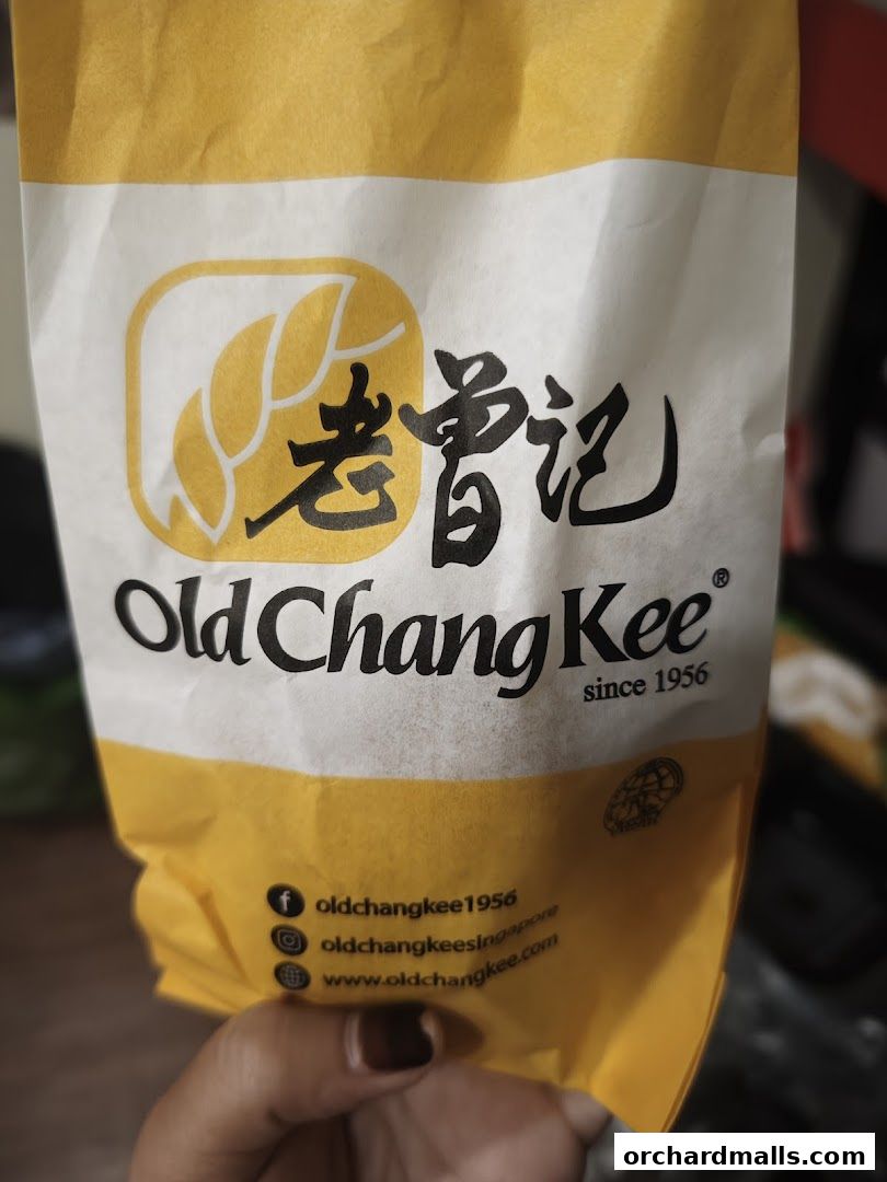 A person holds a yellow and white paper bag with the Old Chang Kee logo and social media handles.