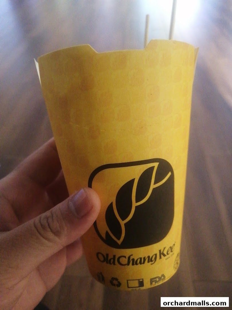 A hand holds a yellow paper cup with the Old Chang Kee logo and branding.