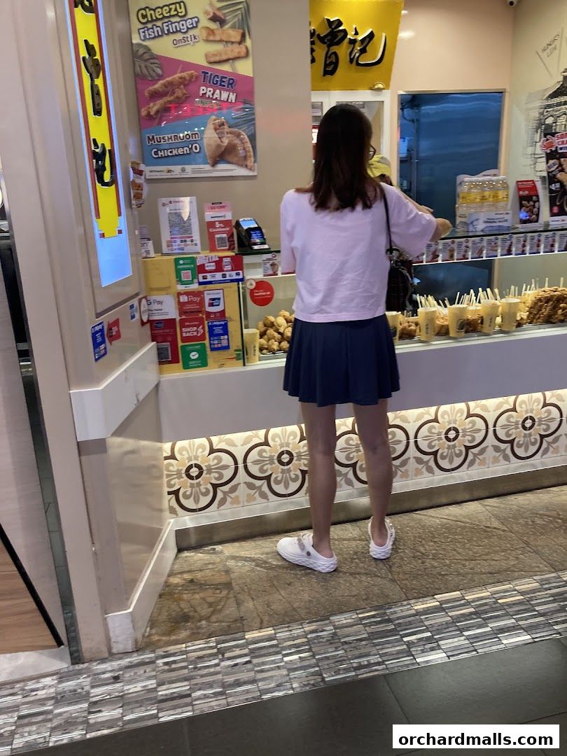 A customer stands at the counter of Old Chang Kee, a food stall with various snacks displayed.