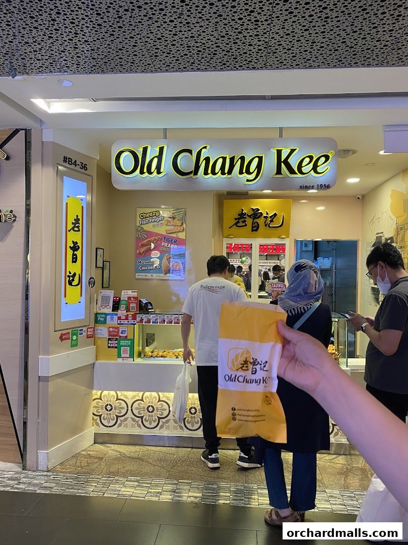 The exterior of an Old Chang Kee shop with customers and signage.
