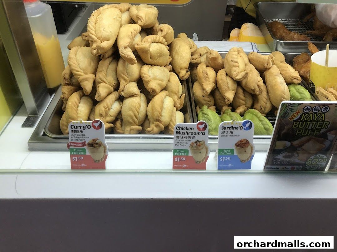 A display of various fried pastries, including curry puffs, chicken mushroom puffs, sardine puffs, and kaya butter puffs.