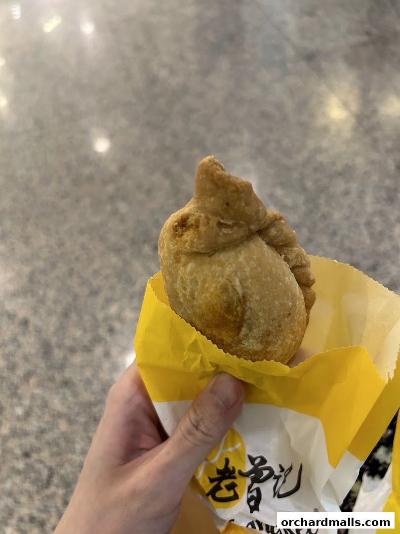 A hand holds a golden-brown curry puff in a yellow Old Chang Kee paper bag.
