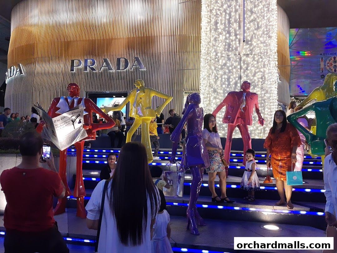 People gather around colorful statues in front of a Prada store decorated with lights.