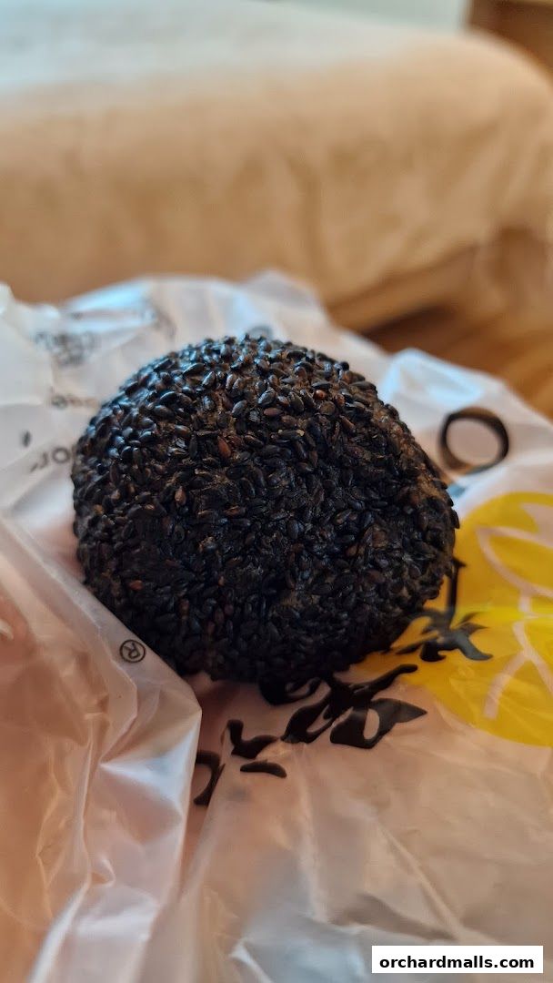 A close-up of a black sesame bun from Old Chang Kee, wrapped in plastic.