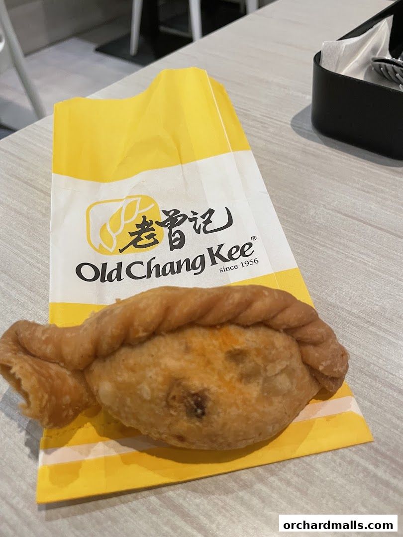 A golden-brown curry puff sits on a yellow Old Chang Kee paper bag.