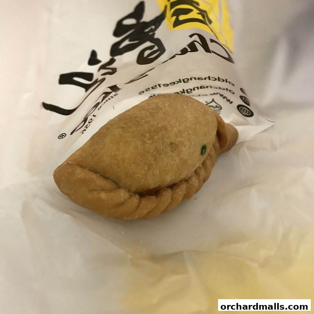 A close-up of a golden-brown curry puff from Old Chang Kee in its packaging.
