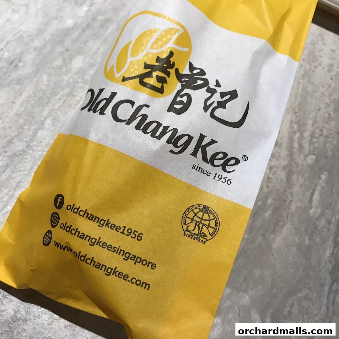 A close-up of a yellow and white paper bag from Old Chang Kee, featuring their logo and social media handles.