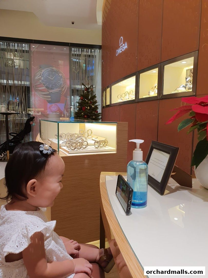 A child sits in front of an OMEGA watch store display with a Christmas tree.