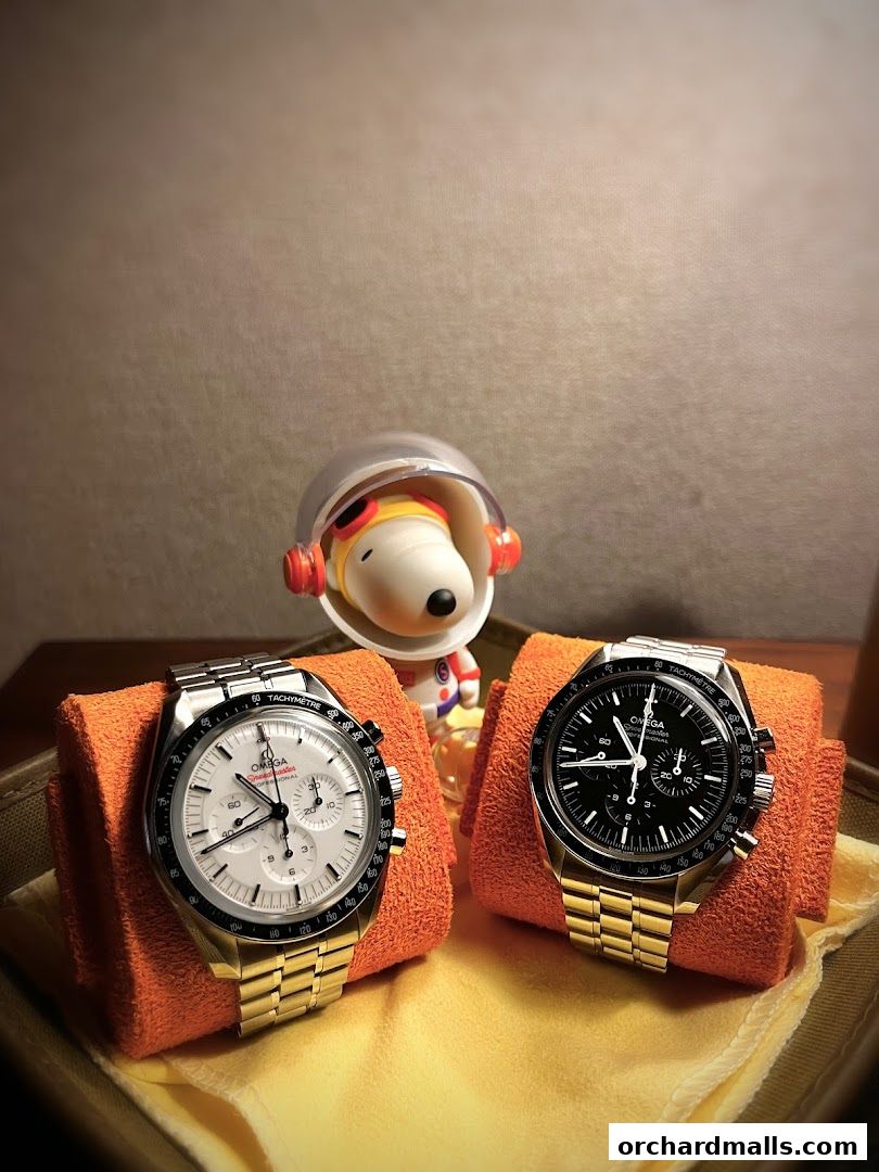 Two OMEGA watches displayed with a Snoopy figurine in an astronaut suit.