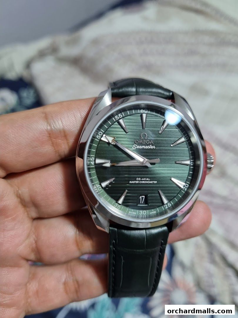 A person holds an OMEGA Seamaster watch with a green dial and a black leather strap.