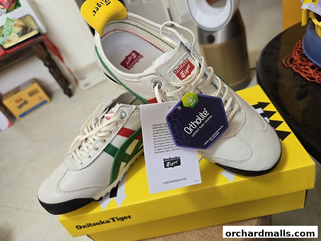 A pair of white Onitsuka Tiger sneakers with green and red stripes on a yellow box.
