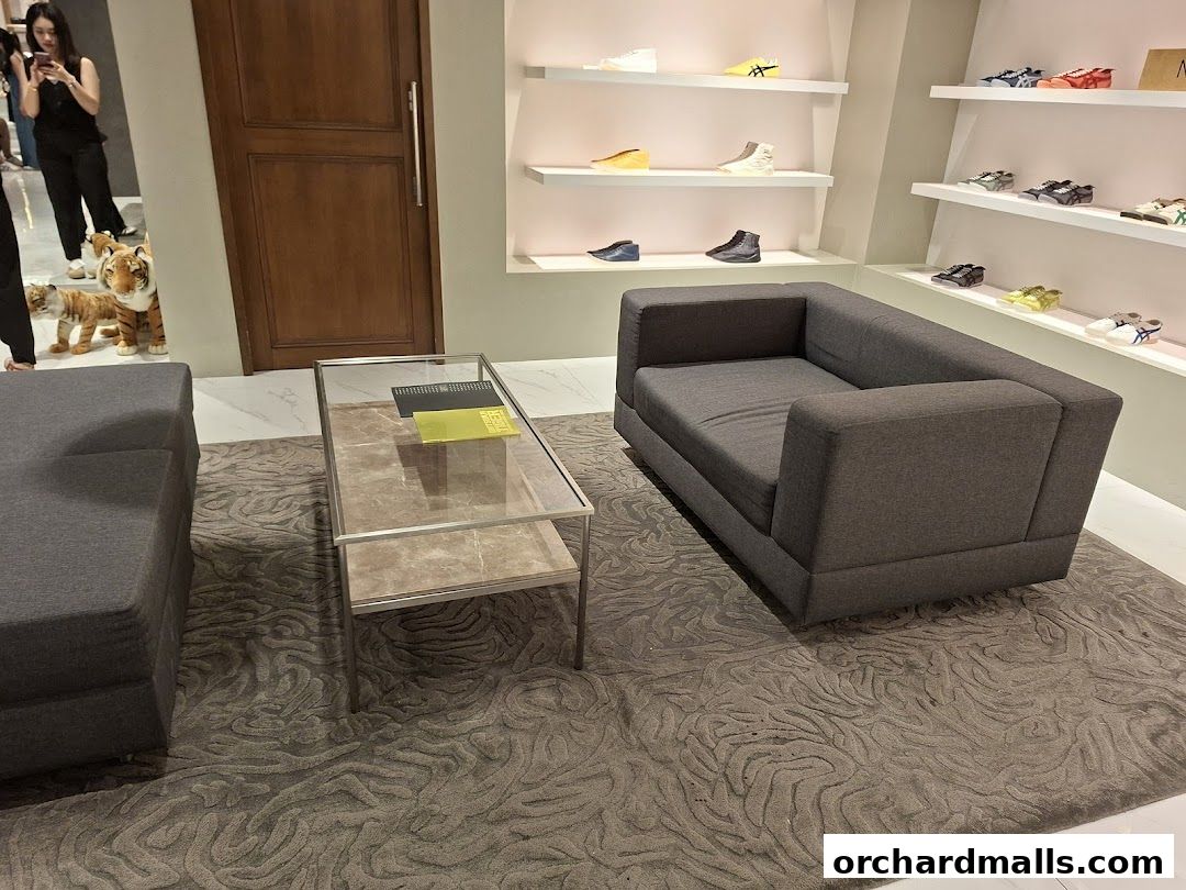 Interior of Onitsuka Tiger shop with sofas, coffee table, and shoes displayed on shelves.