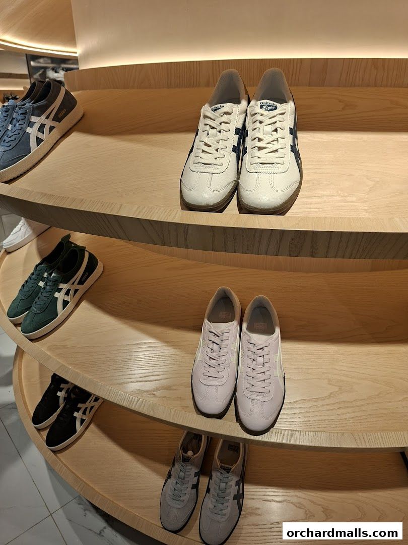 A display of various Onitsuka Tiger sneakers on tiered wooden shelves.