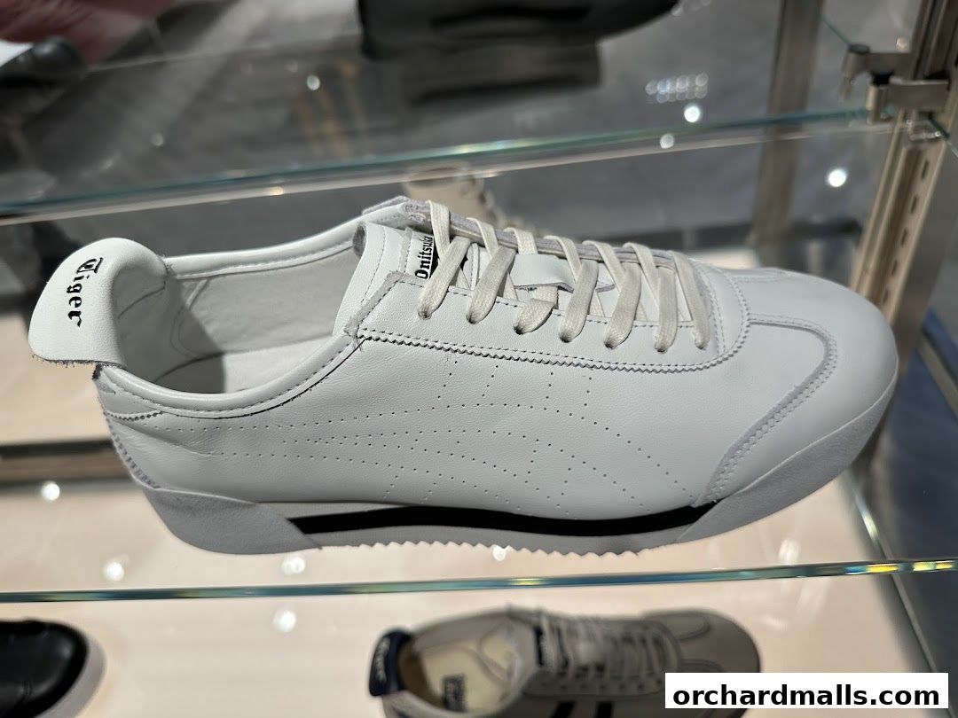 A close-up view of a white Onitsuka Tiger sneaker displayed on a glass shelf.