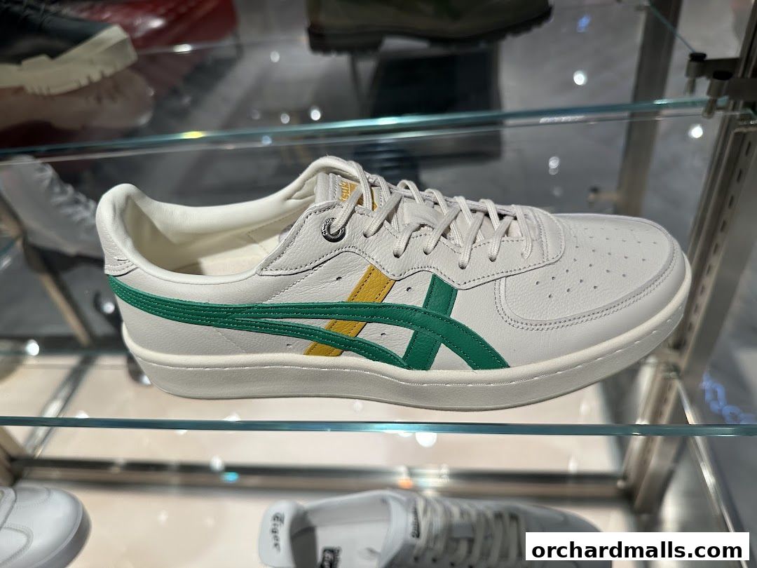 A white Onitsuka Tiger sneaker with green and yellow stripes displayed on a shelf.
