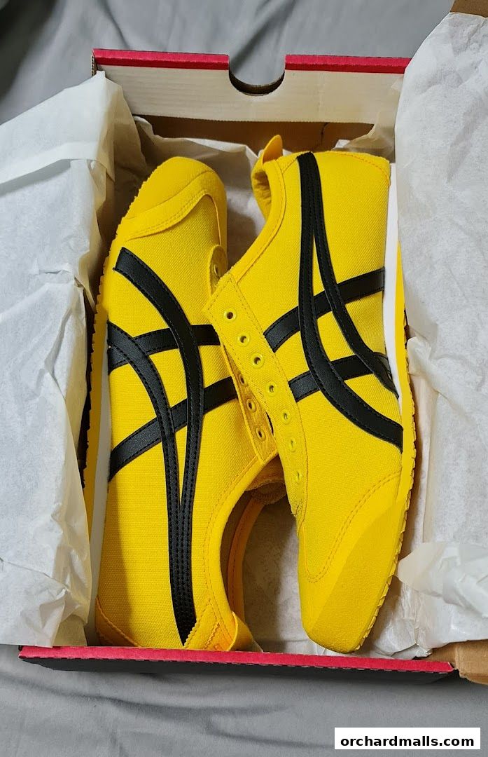 A pair of bright yellow Onitsuka Tiger sneakers with black stripes inside a shoebox.
