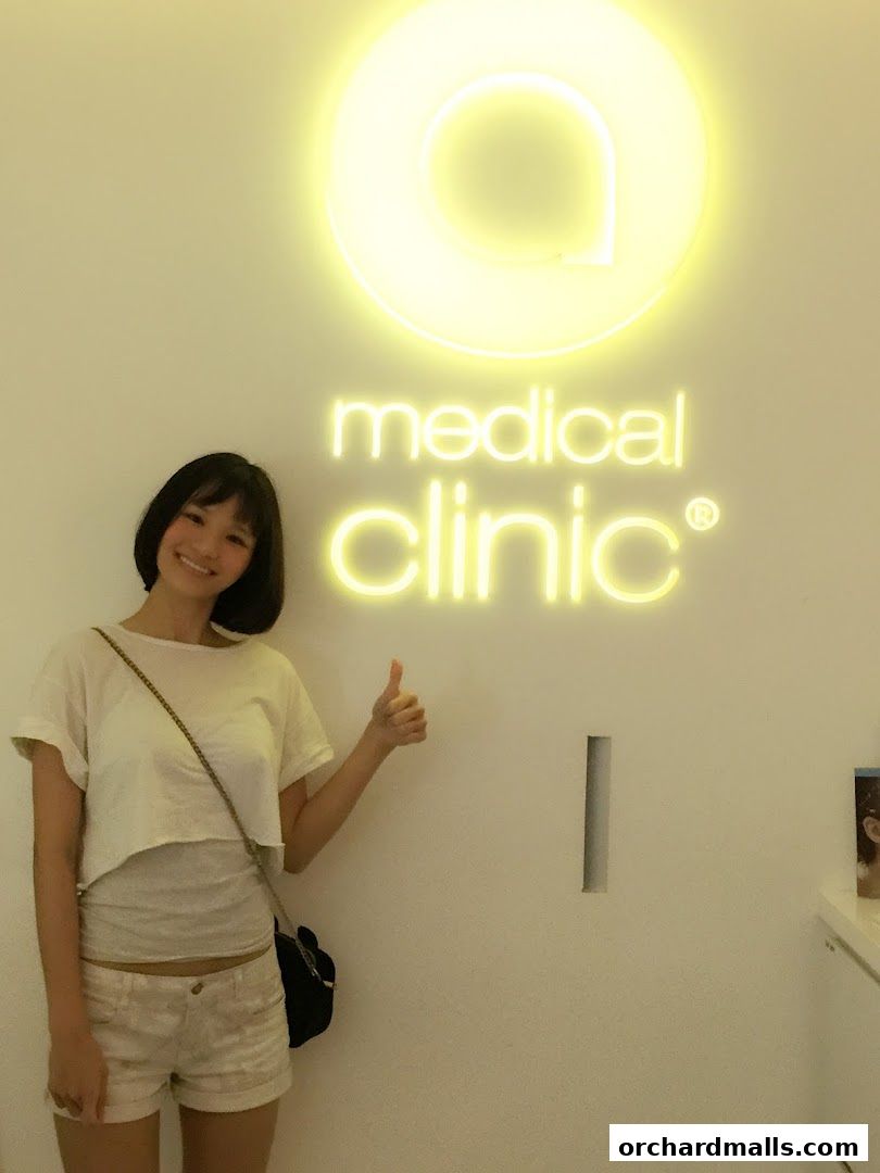 A woman gives a thumbs up in front of a glowing neon sign for 'medical clinic'.
