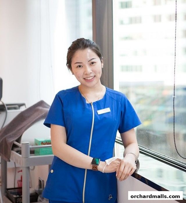 A smiling woman in a blue uniform stands by a window at Only Aesthetics.