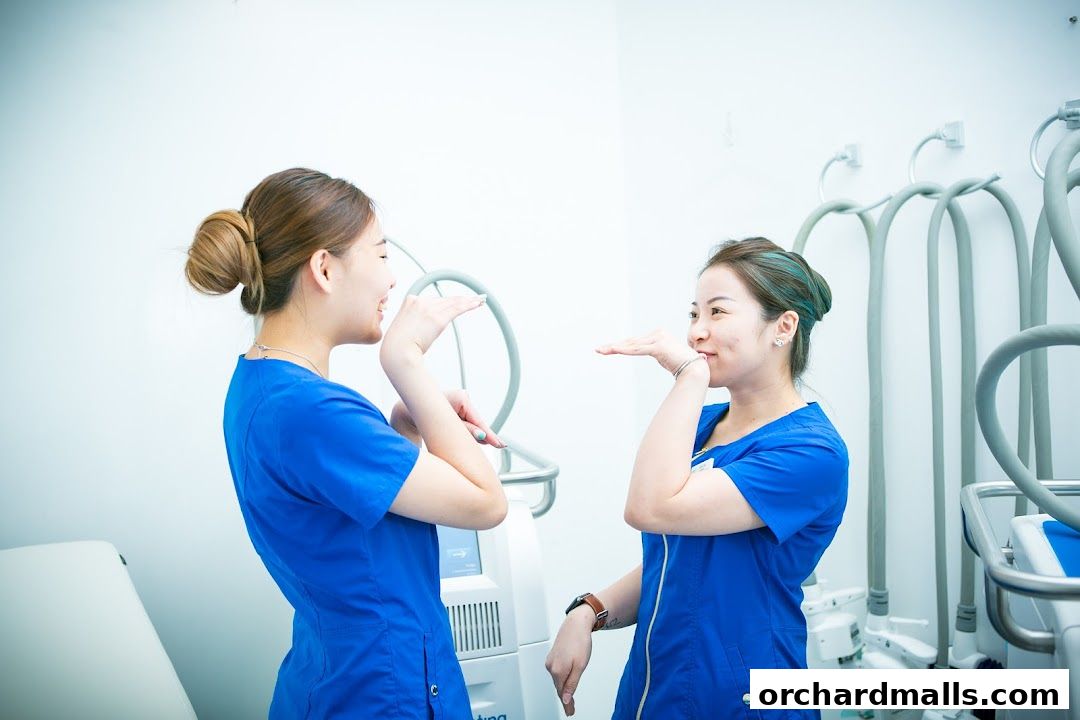 Two women in blue scrubs playfully pose with their hands in front of their faces.