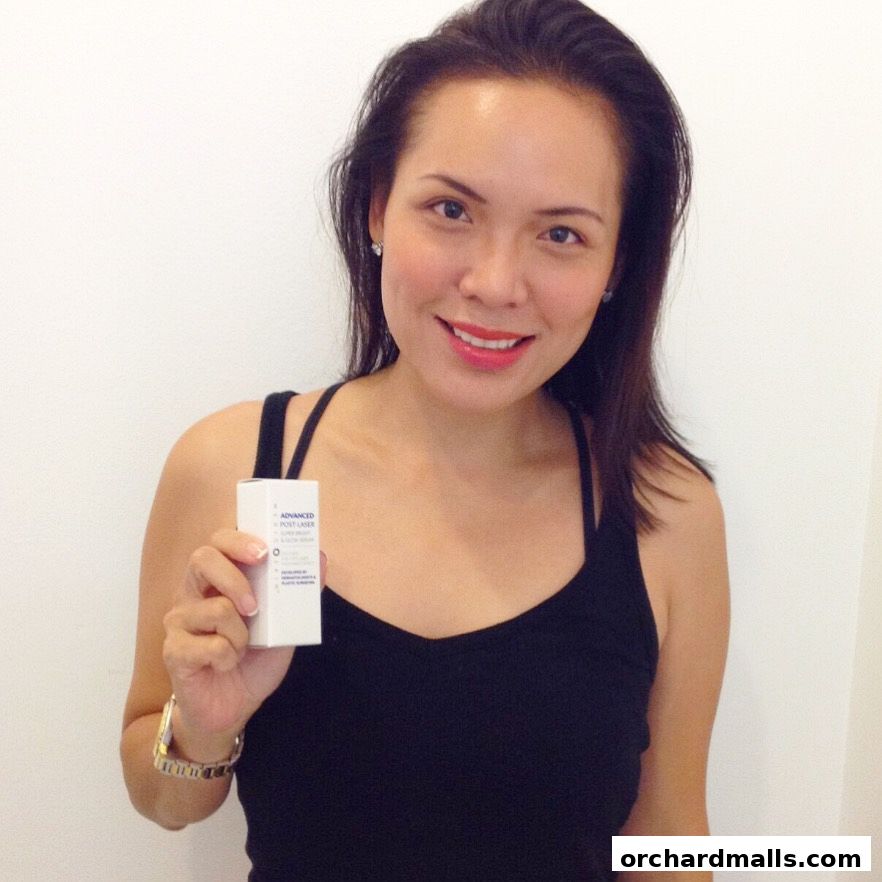 A woman holds a small white box with text on it, smiling at the camera.