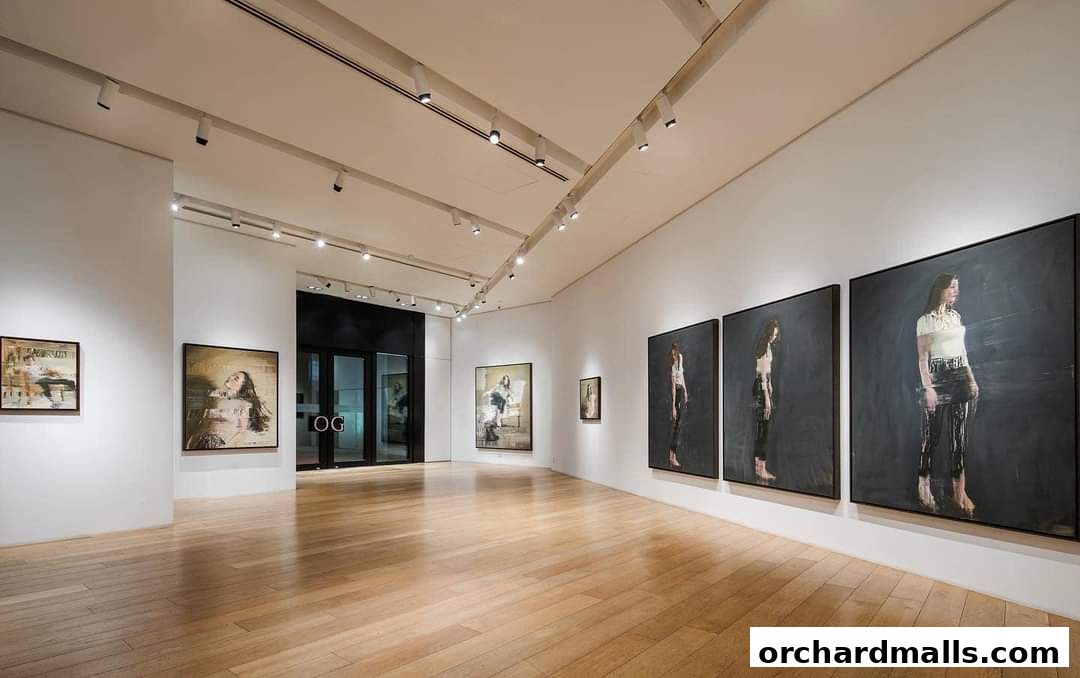 Interior view of an art gallery with paintings displayed on white walls and wooden floors.