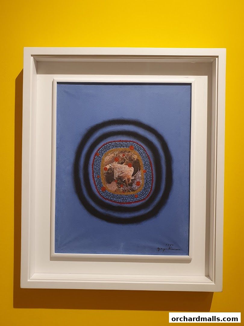 A framed artwork with a blue background featuring a circular design and a signature.