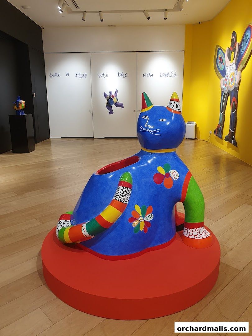 A vibrant, colorful sculpture of a cat is displayed in an art gallery setting.