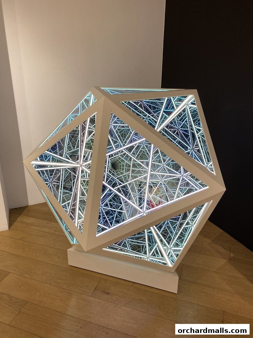 An illuminated geometric sculpture with an infinity mirror effect on a wooden floor.