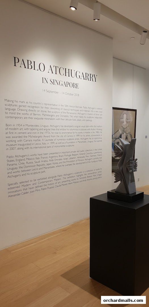 An art exhibition featuring sculptures and text panels on a white wall.