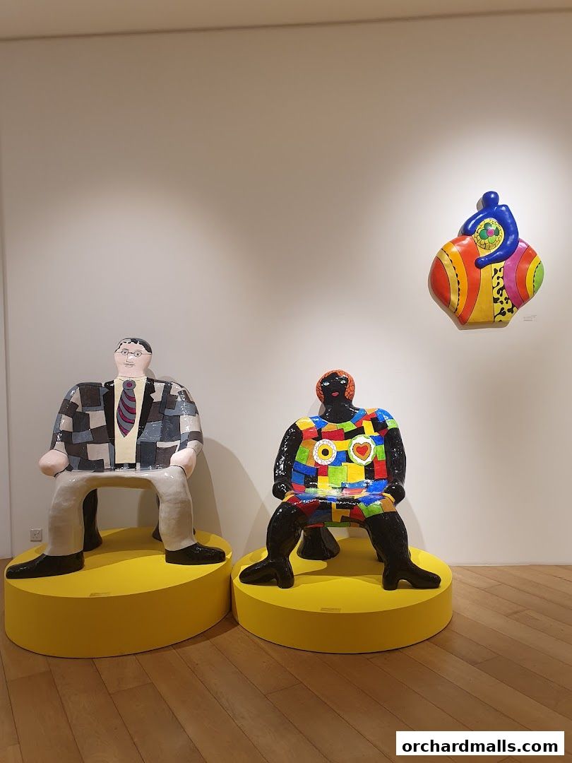 Two colorful, artistic sculptures are displayed on yellow pedestals in a gallery setting.