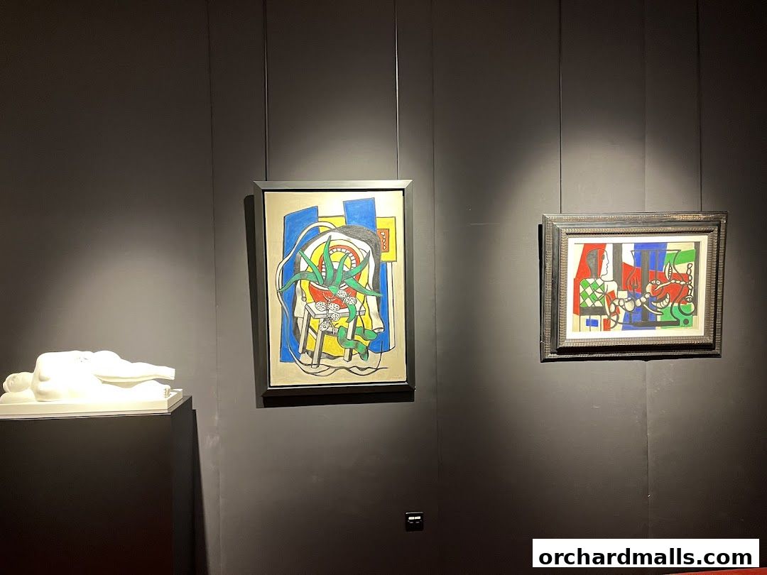 A white sculpture and two colorful paintings displayed on a dark wall in an art gallery.