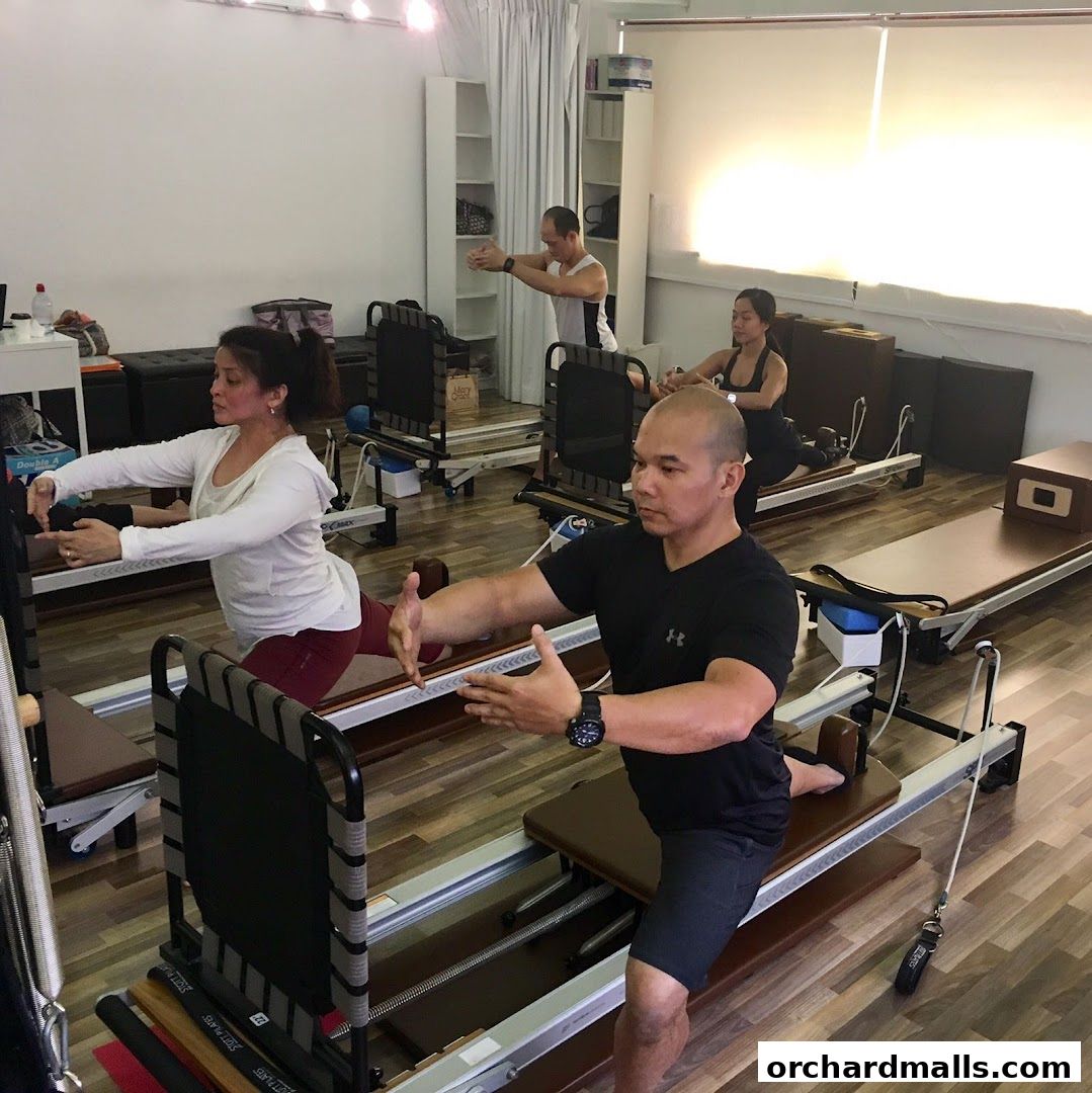 People practicing Pilates on reformers in a bright studio with wooden floors.