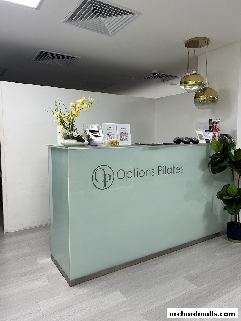 The reception desk of Options Pilates Studio, featuring a logo, floral arrangement, and decorative lighting.